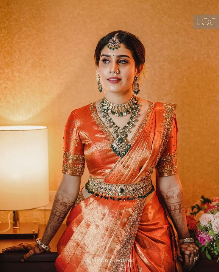 a woman in an orange sari standing next to a lamp