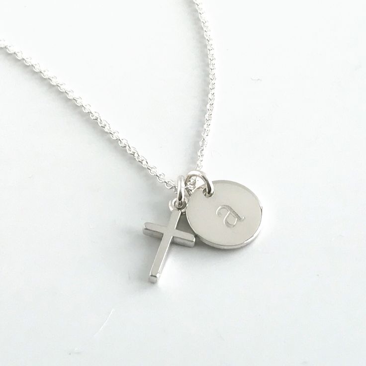 Commemorate a baptism, first communion or another special date with this tiny cross necklace personalized with a dainty initial charm. This cross necklace features a sterling silver cross that measures approximately 1/2 inch, along with a sterling silver round charm that can be engraved with one initial. The chain is also sterling silver and is available in lengths for 15 - 20 inches. Your new necklace will come in a box, ready for gift giving. More Christian jewelry https://www.etsy.com/shop/Au Personalized Dainty Jewelry For First Communion, Silver Cross Pendant Necklace For Birthday, Dainty Personalized Jewelry For First Communion, Personalized Sterling Silver Jewelry For Baptism, Minimalist Personalized Cross Necklace, Silver Cross Necklaces With Name Detail, Personalized Dainty Cross Necklace, Classic Cross Necklace For Baptism, Silver Name Necklace With Cross Pendant