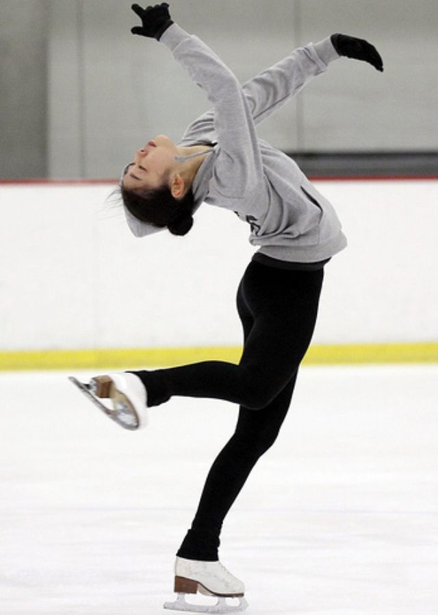 a woman skating on an ice rink with her arms in the air and one leg up