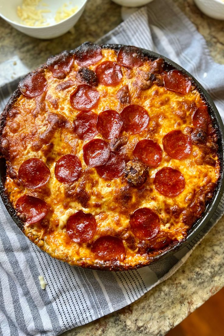 a pepperoni pizza sitting on top of a table next to bowls and utensils