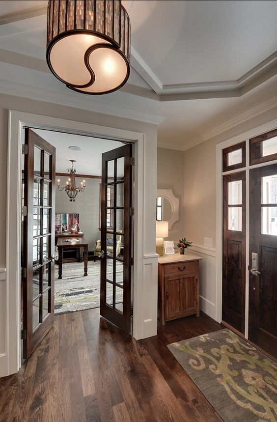 an entry way with wooden floors and two doors leading to another room that has a chandelier hanging from the ceiling