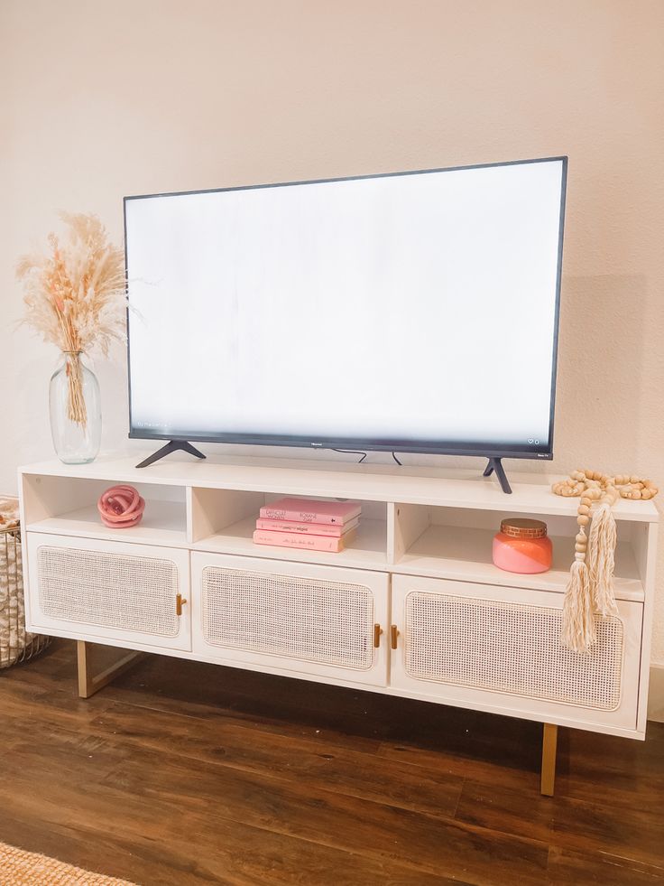 a flat screen tv sitting on top of a white entertainment center next to a vase filled with flowers