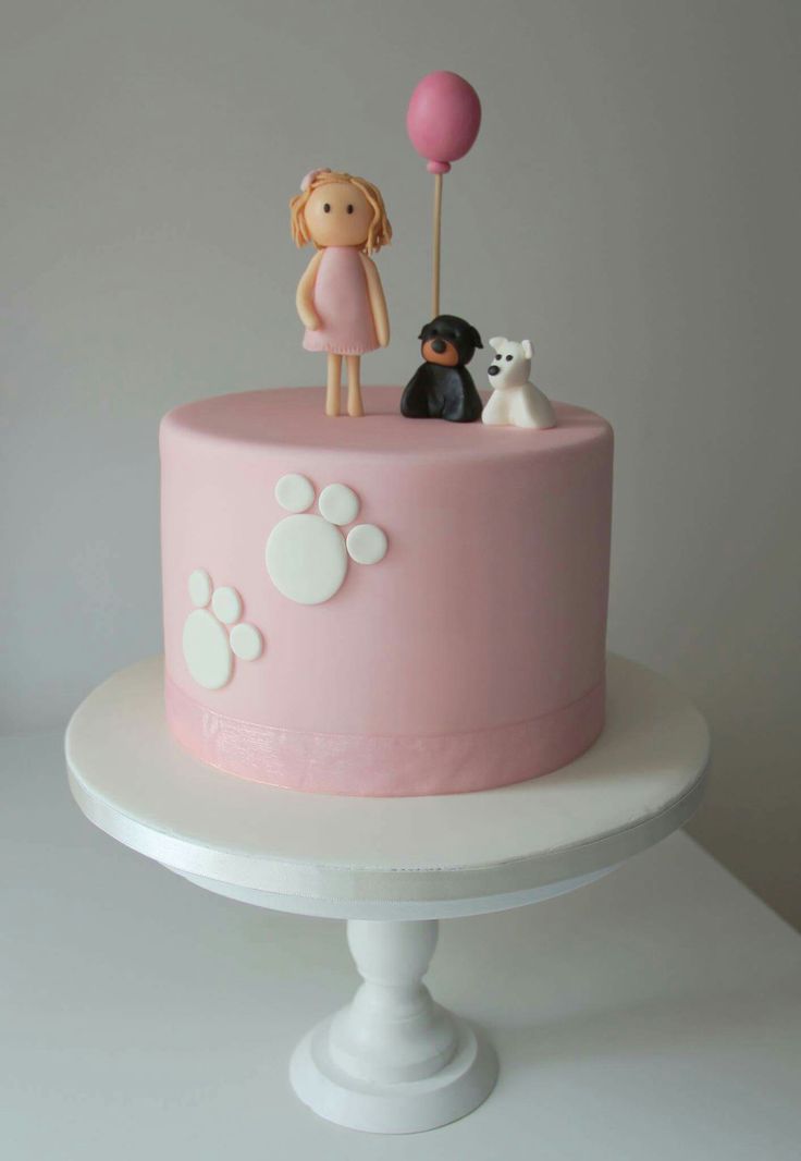 there is a pink cake decorated with dogs and people on top, along with a balloon