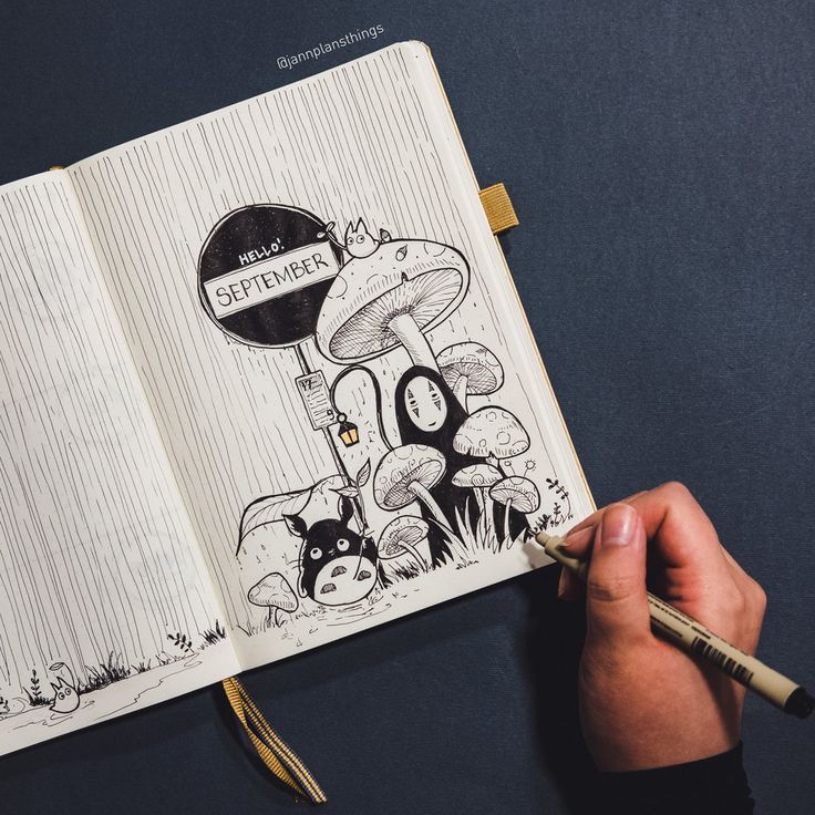 a hand holding a pencil drawing an open book with cartoon characters on it and mushrooms in the background