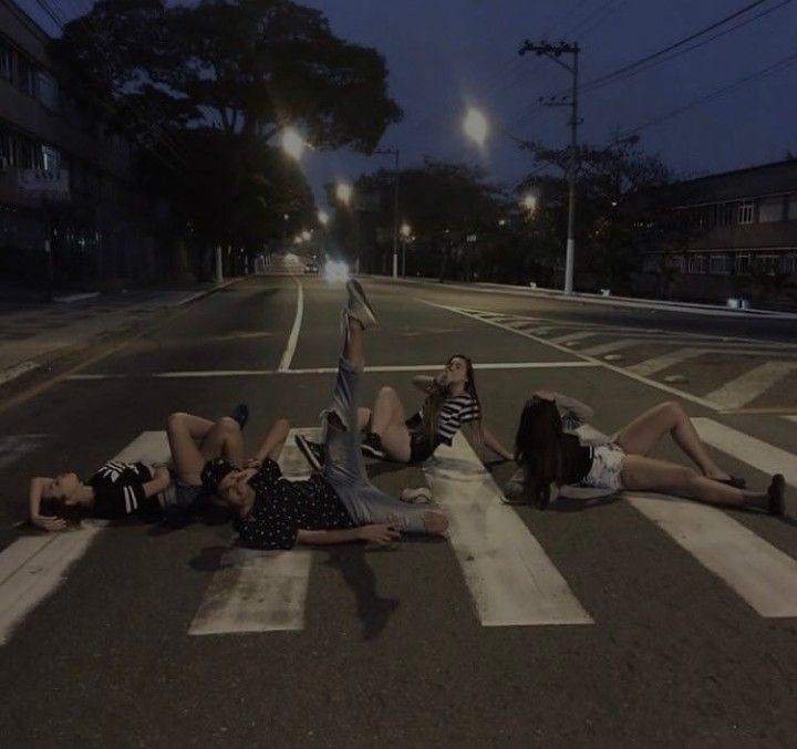 three people laying on the ground in the middle of an empty street at night time