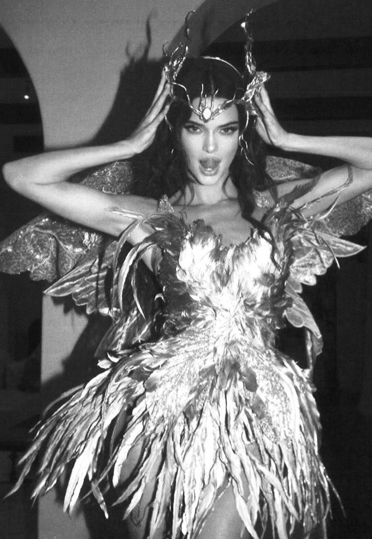 a woman in a costume with feathers on her head and hands behind her head, posing for the camera