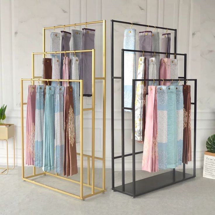 three racks with clothes hanging on them in front of a mirror and potted plant