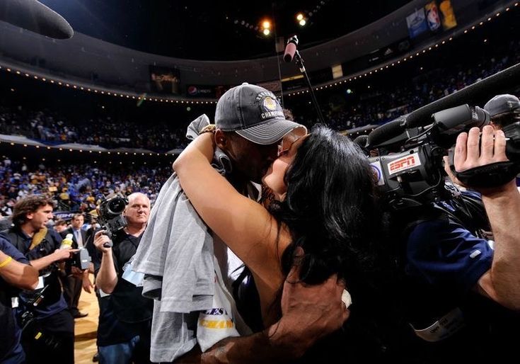 a man and woman kissing in the middle of a basketball court with cameras around them