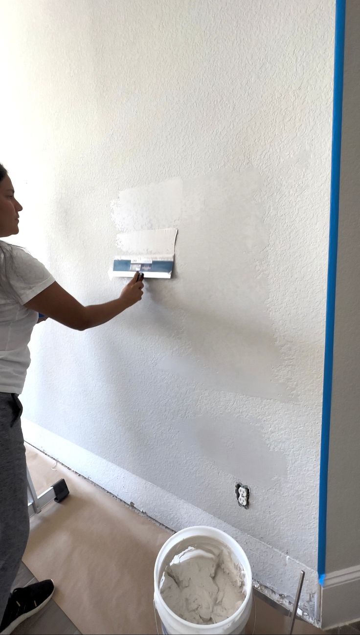 a woman is painting the wall with white paint