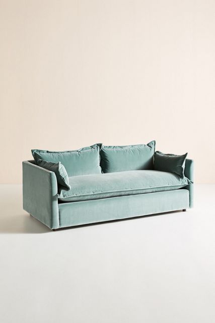 a blue couch sitting on top of a white floor next to a wall with two pillows