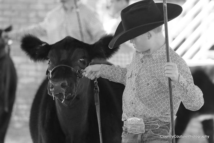 a little boy standing next to a cow wearing a cowboy hat and holding an umbrella