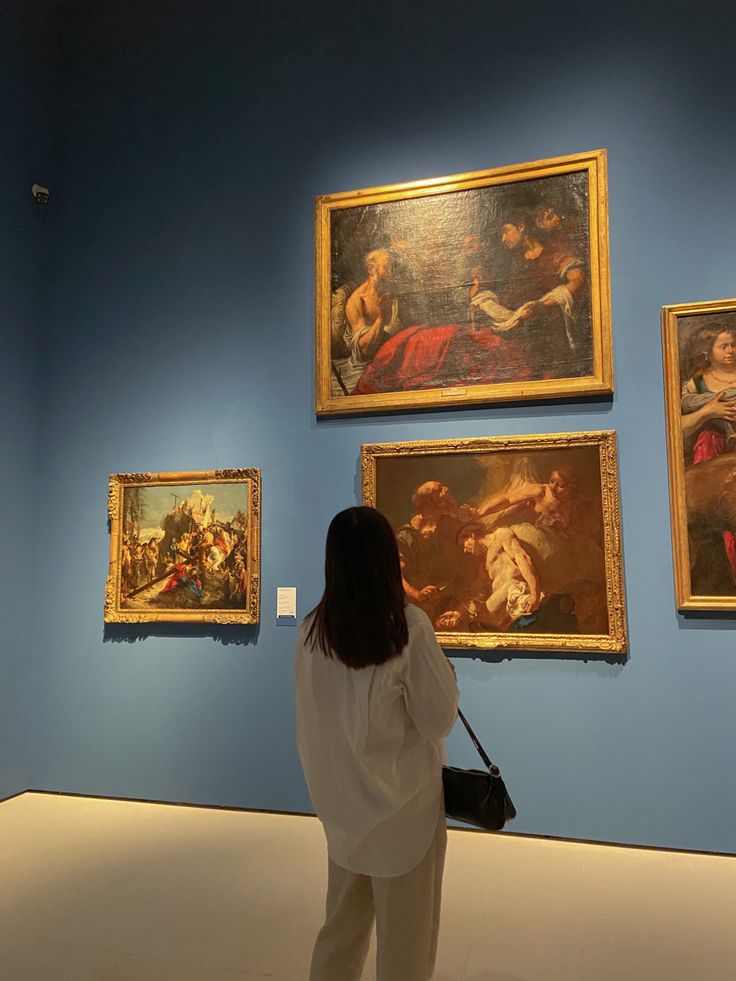 a woman is looking at paintings on the wall in an art museum with blue walls