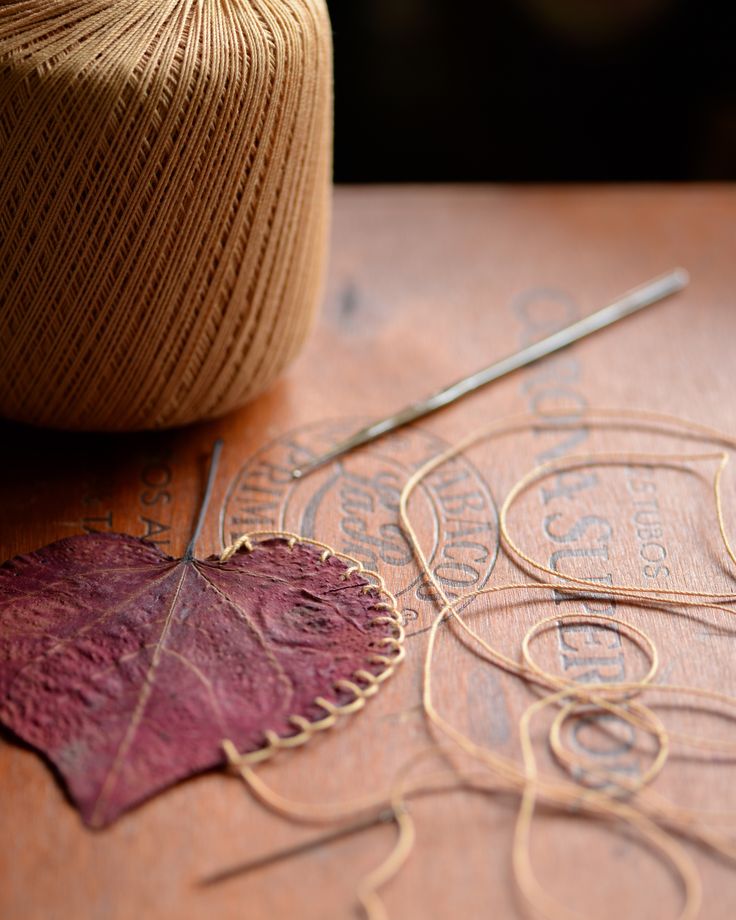 a close up of a piece of wood with yarn on it and a ball of thread next to it