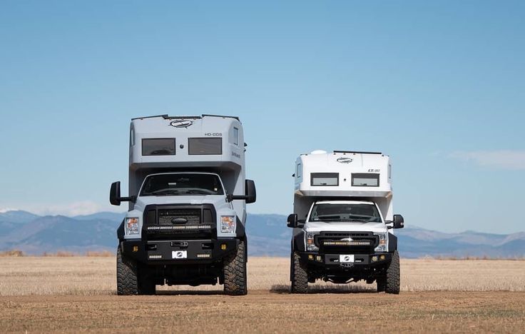 two trucks with campers on the back parked in an open field