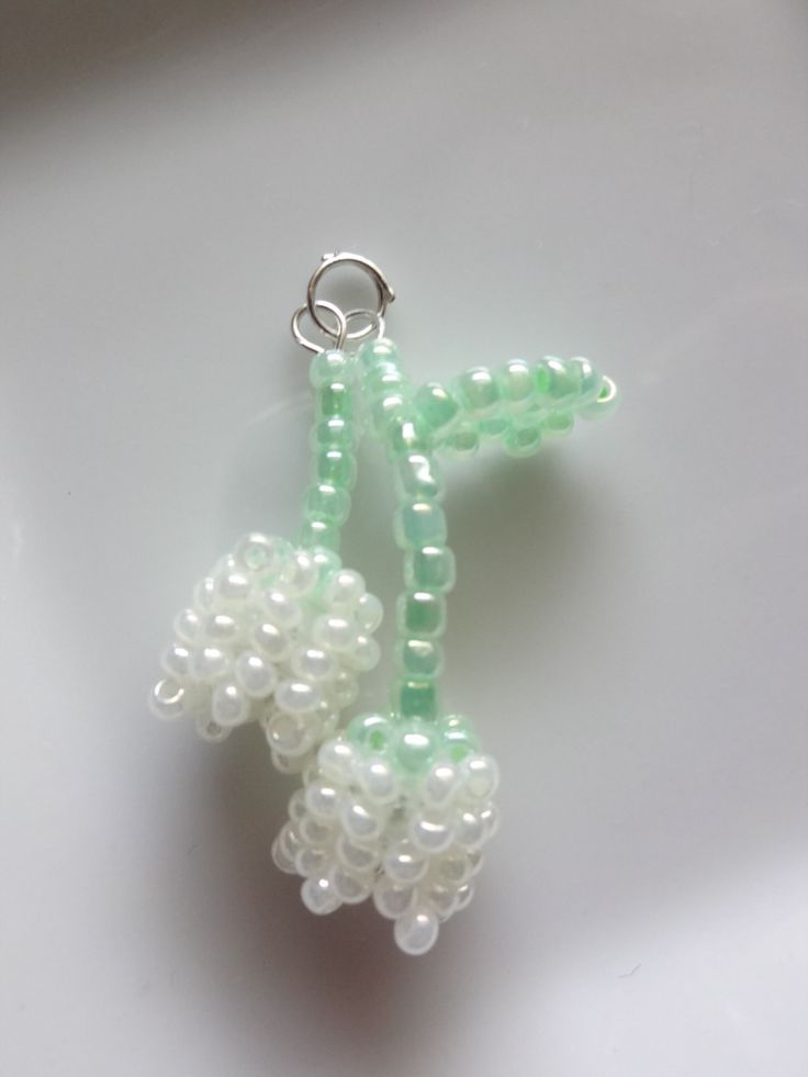 two beads are attached to a keychain on a white surface, one is green and the other is white