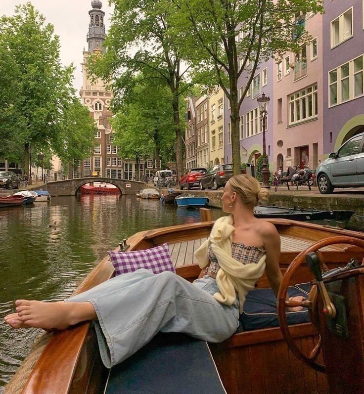 a woman sitting on the back of a boat in a canal next to tall buildings