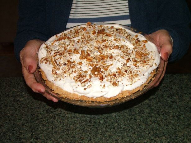 a person holding a pie with white frosting and pecans on top in their hands