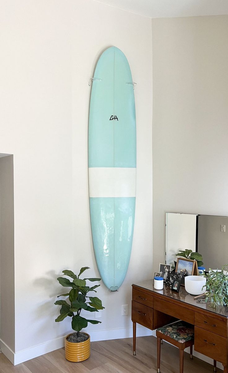 a blue surfboard hanging on the wall in a room with a desk and mirror