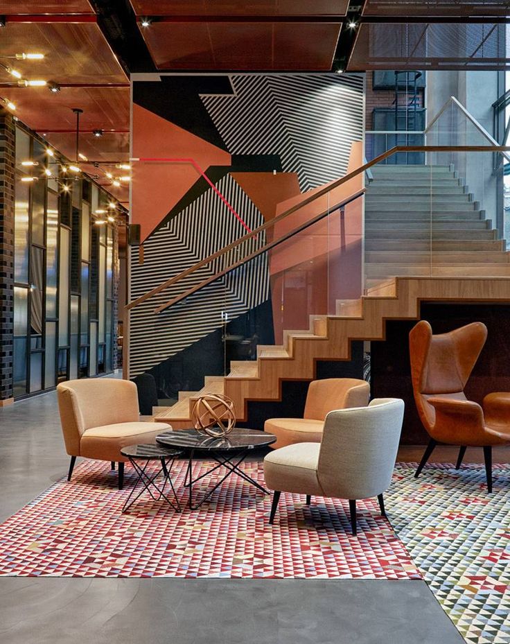 two chairs and a coffee table in front of a stair case with an abstract design