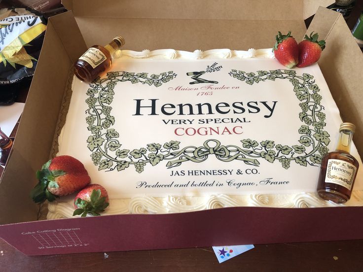 a cake in a box with some strawberries on the side and two bottles of hennessy very special cognac