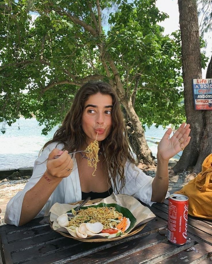 a woman sitting at a picnic table eating food from a plate with chopsticks