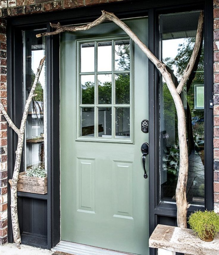 a green front door with black trim and two trees in the foreground, on a brick building