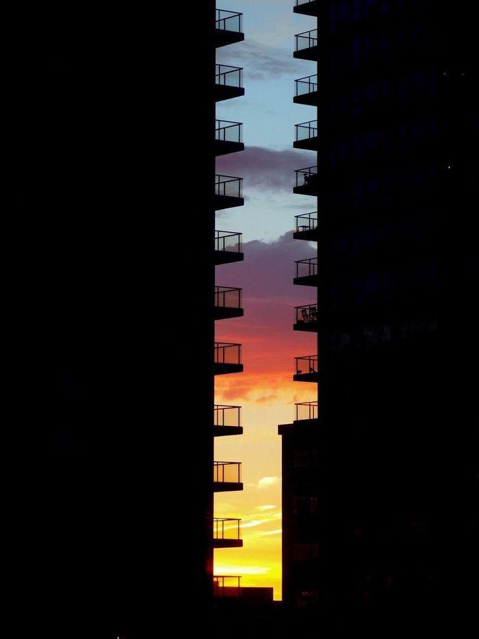 the silhouette of two tall buildings against a colorful sky at sunset or sunrise, with balconies and balconies on either side