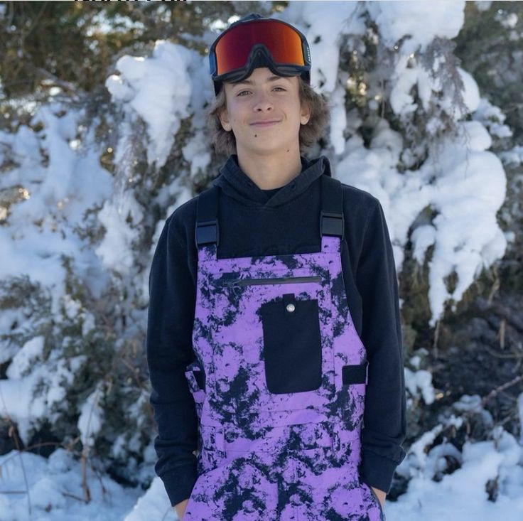 a young man standing in front of snow covered trees