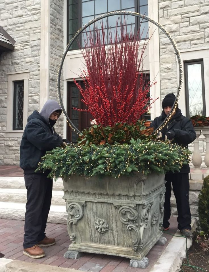 two men standing next to a large potted planter with red flowers in it