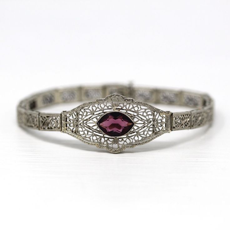 "Gorgeous antique circa 1920s Art Deco era 10k white gold and simulated amethyst bracelet! This phenomenal statement bracelet features intricate nature inspired filigree, with a marquise cut simulated amethyst purple glass stone in the center. The bracelet secures with a box clasp, and has a push tab opener. A stunning piece of fine Art Deco era jewelry, featuring February's birthstone color!  ERA - Circa 1920s - Art Deco  METAL / MATERIAL - 10k white gold, glass  MARKINGS / HISTORY - Bracelet is marked \"10k\"  CONDITION - Good vintage condition. White gold metal has been professionally polished & cleaned. Simulated amethyst stone is secure in setting. Age appropriate patina & wear remains. Amazing antique bracelet!  MEASUREMENTS - Length: 6 1/2 inches, Width (widest area): 5/8 inches, We Vintage White Gold Filigree Jewelry, Vintage Round Diamond Cut Bracelet, White Gold Filigree Jewelry For Vintage Events, Antique Filigree White Gold Jewelry, Antique White Gold Filigree Jewelry, Elegant Purple Bracelets For Wedding, Elegant Purple Wedding Bracelets, Vintage Silver Bracelets With Diamond Cut, Vintage Filigree Jewelry For Vintage Events