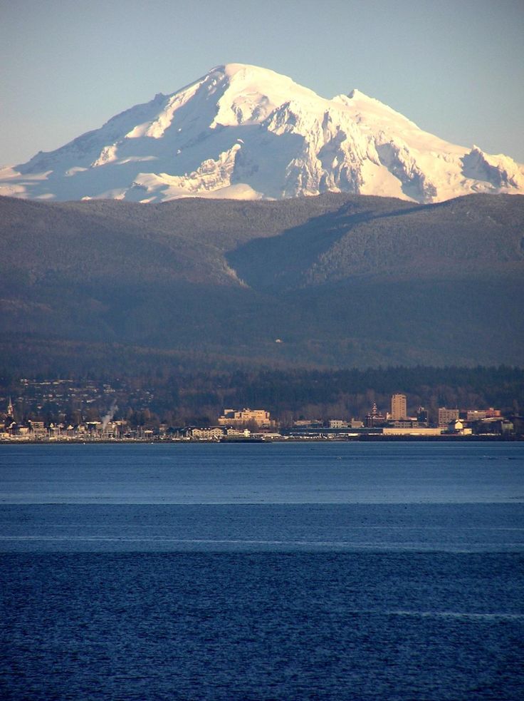 a large snow covered mountain in the distance with blue water and buildings on it's sides