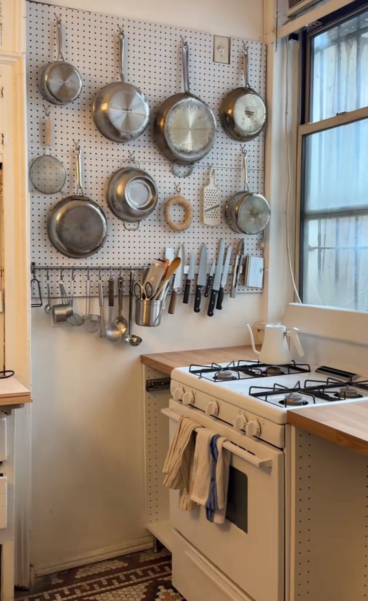 pots and pans are hanging on the wall next to an oven in a kitchen