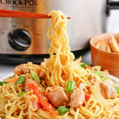 noodles with meat and vegetables being lifted from an instant pot by chopsticks in front of the pressure cooker