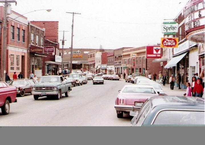 cars are driving down the street in front of shops and businesses on a cloudy day