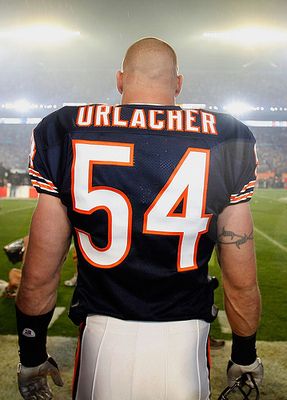 the back of a football player wearing an orange and black uniform at a game with fans in the stands