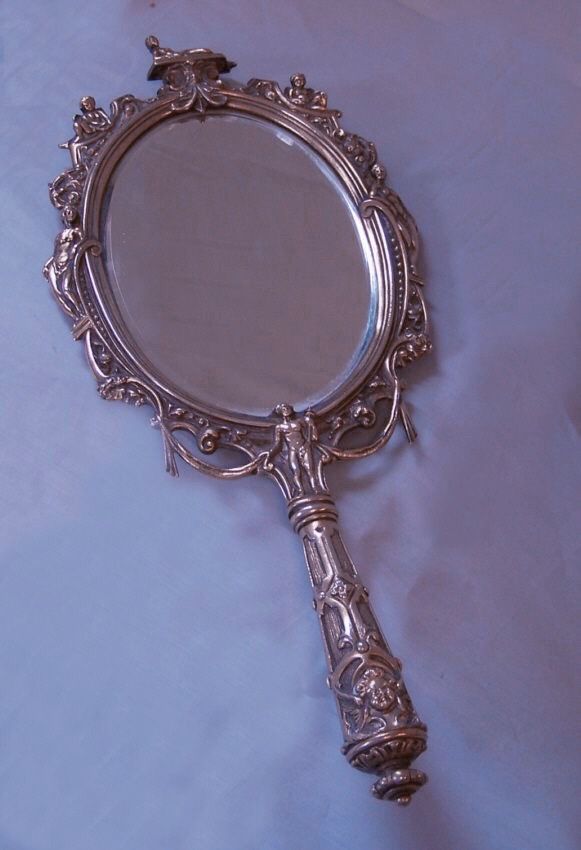 an ornate silver mirror on a white sheet with a bird perched on the top of it