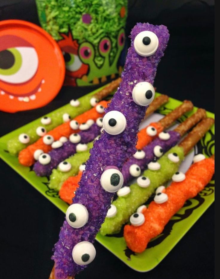 some food sticks with googly eyes and carrot sticks sticking out of them on a green plate