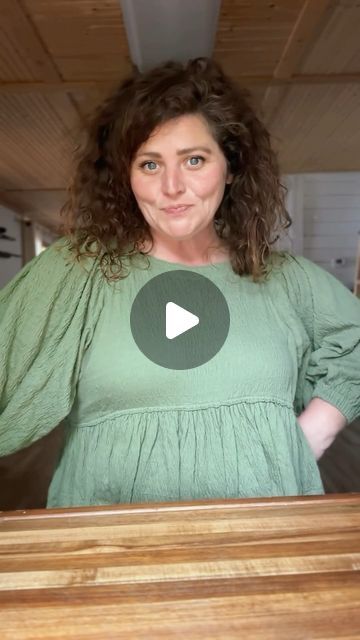 a woman standing in front of a wooden table with her hands on her hips and looking at the camera