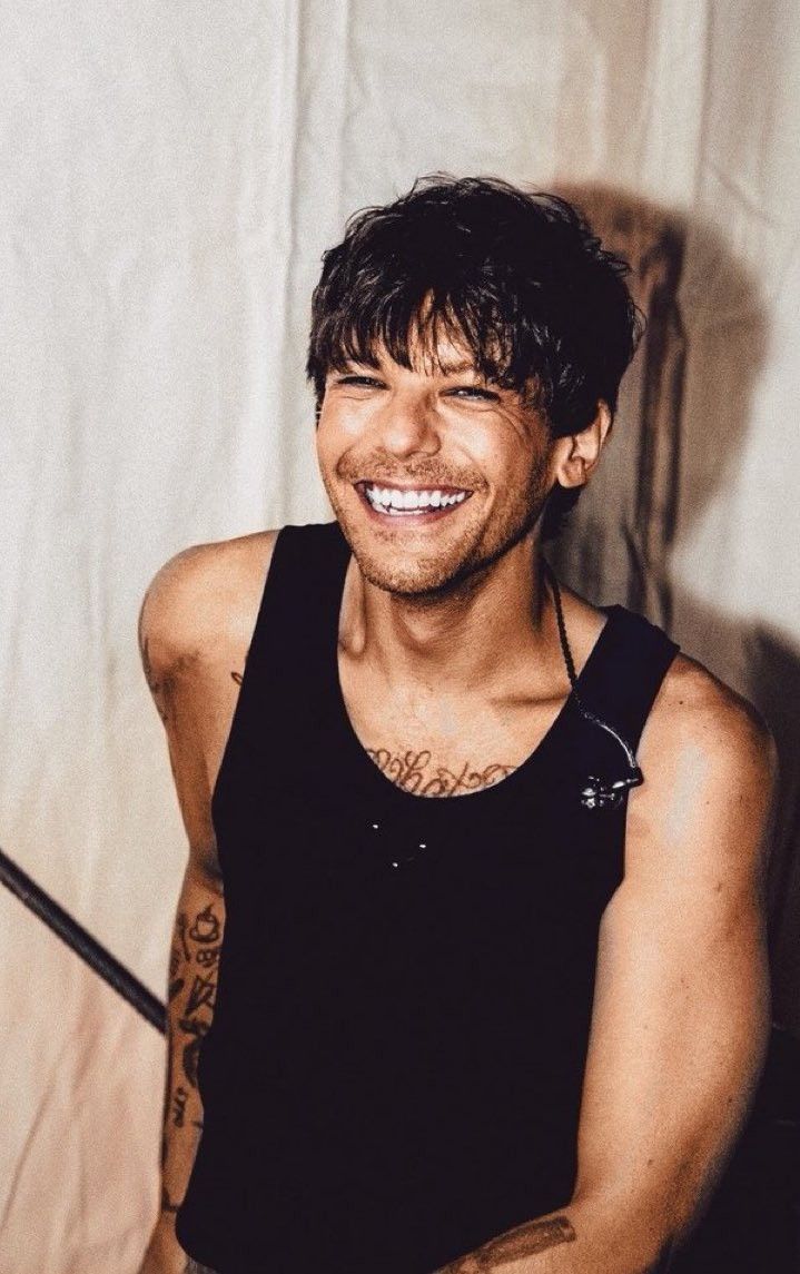 a smiling man with tattoos on his arm and chest, wearing a black tank top