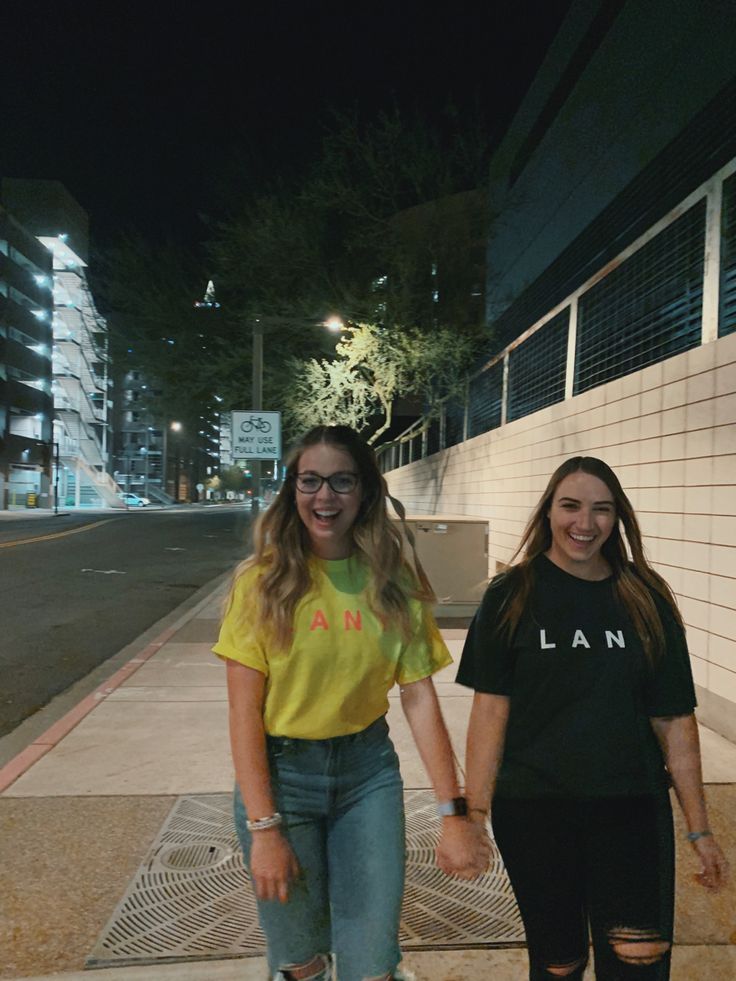 two girls are walking down the sidewalk holding hands and smiling at the camera while wearing glasses