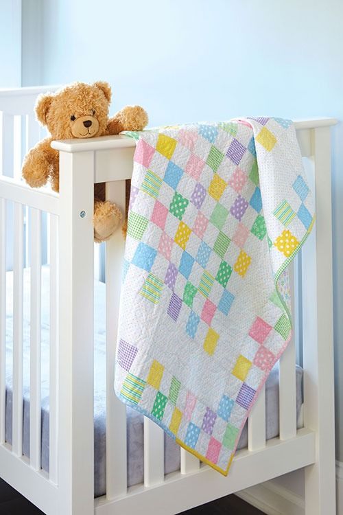 a teddy bear sitting on top of a white crib next to a baby quilt