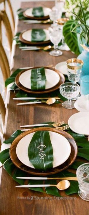 the table is set with green and white plates, silverware, and palm leaf napkins