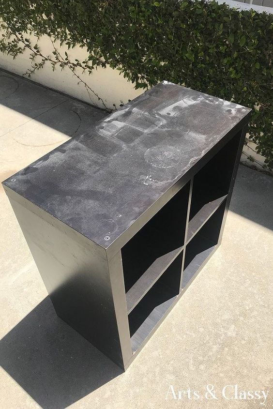 a black and silver bookcase sitting on top of a cement floor next to a bush