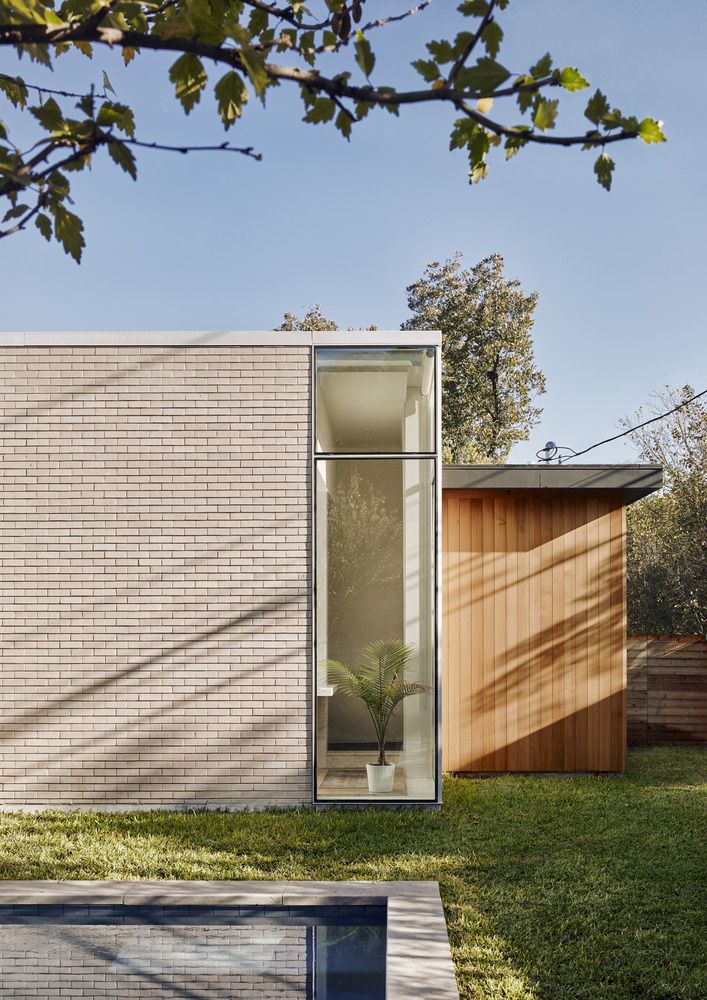 a brick house with a pool in the foreground and grass on the other side