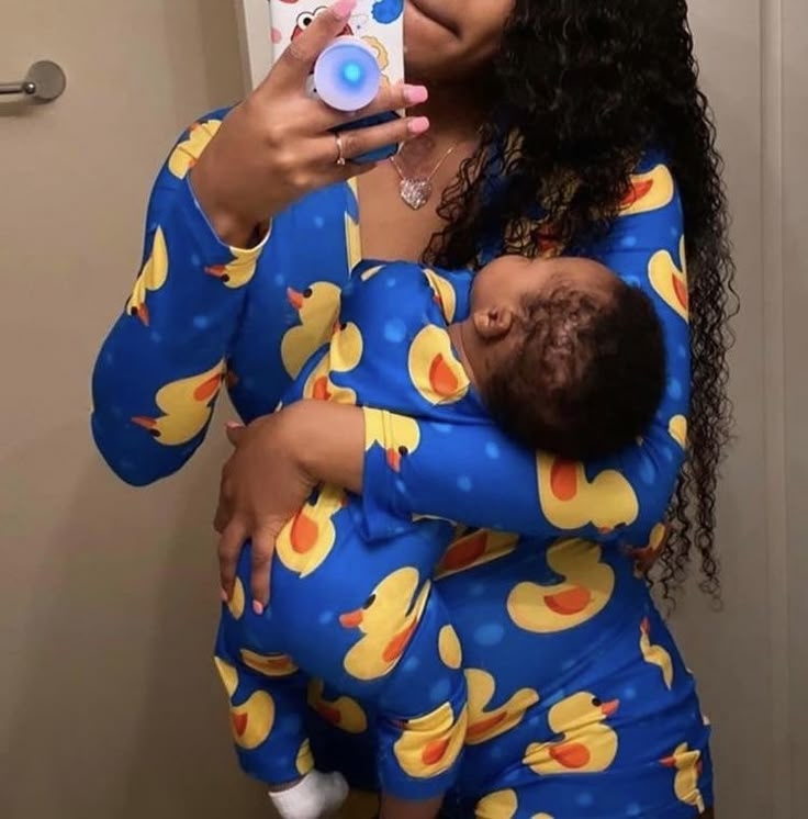 a woman holding a baby taking a selfie in front of a mirror with her cell phone