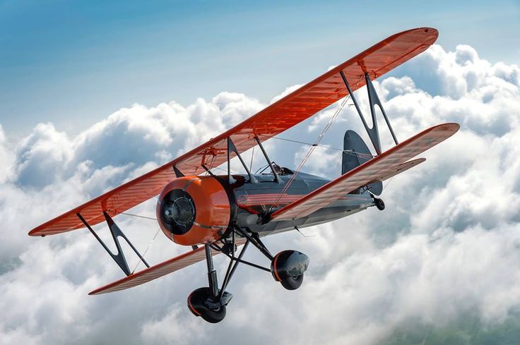 an orange biplane flying above the clouds