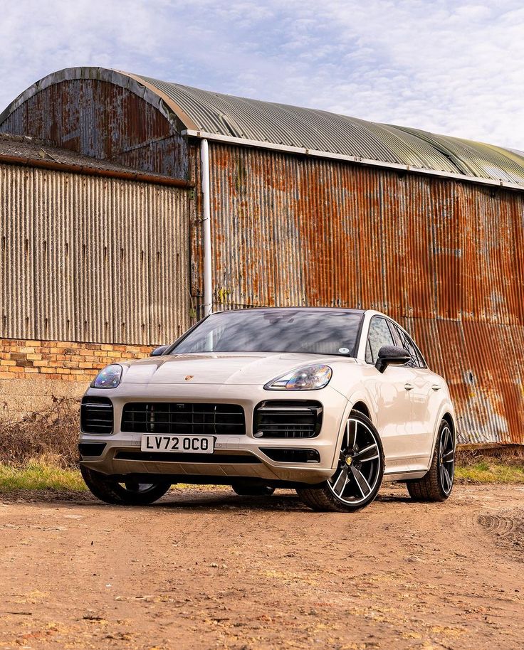 a white porsche cayen is parked in front of an old barn