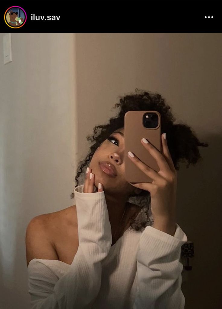 a woman taking a selfie with her cell phone in front of her face while wearing a white sweater