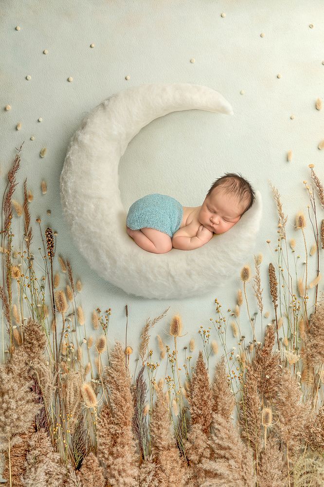 a baby sleeping on top of a white moon in the middle of some tall grass