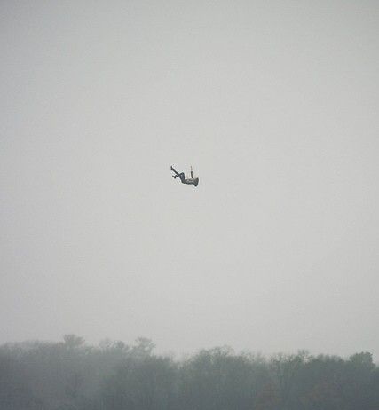 two airplanes are flying in the sky over some trees on a foggy, gray day